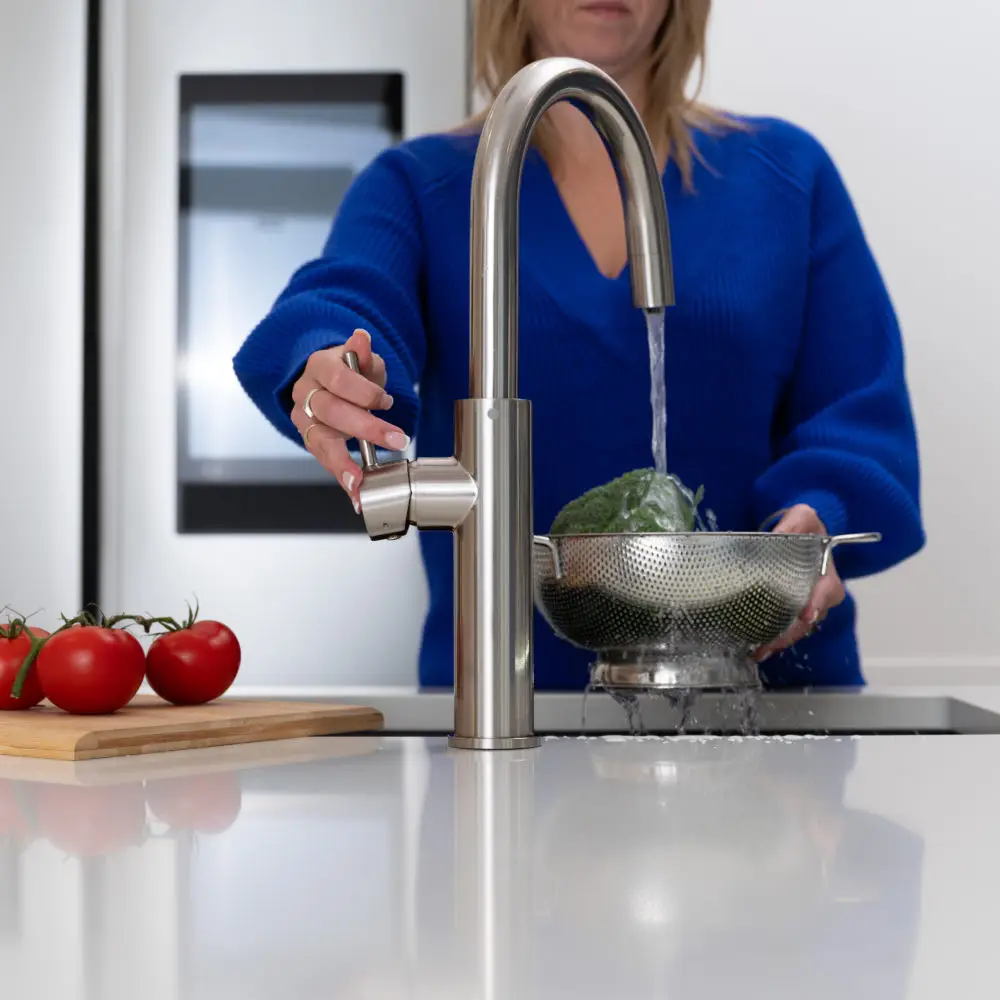 A Woman Washing Vegetables Under A Faucet